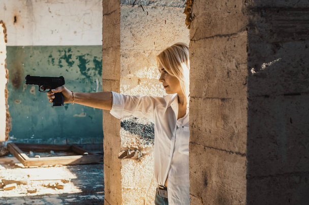 Mujer con camisa blanca dispara una pistola en un edificio abandonado
  - Foto, imagen