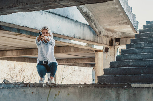 Woman in a white shirt squats on concrete steps, shoots a gun - 写真・画像