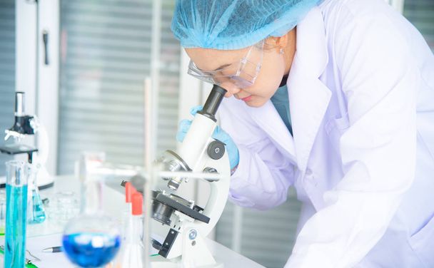 Asian woman scientist, researcher, technician, or student conducted research or experiment by using microscope which is scientific equipment in medical, chemistry or  biology laboratory - Photo, Image