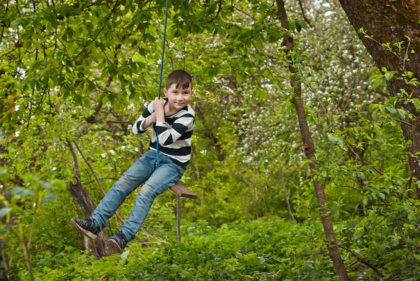 Children are riding a swing in the park. Guys on a homemade swing from ropes and boards. Light blur as an artistic effect of motion. - Foto, afbeelding