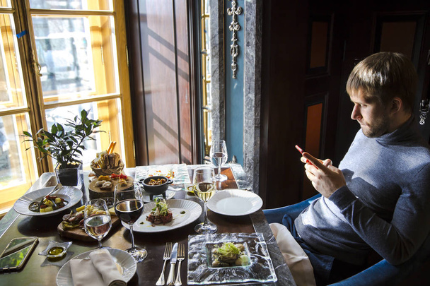 Geschäftsessen. Zeitgenössischer junger Mann in elegantem Restaurant tippt per Handy eine SMS. - Foto, Bild