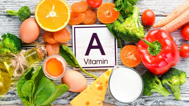 Foods containing natural Vitamin A: broccoli, carrots, milk, cheese, spinach, apricots, parsley, tomatoes. On a white wooden background. Top view. - Foto, imagen