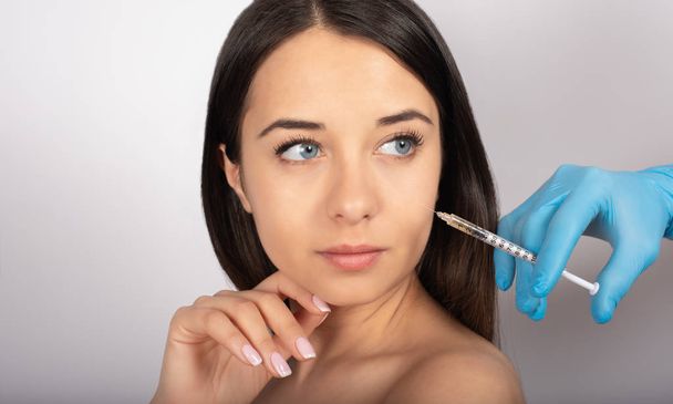 beautiful brunette girl with blue eyes, white background, beauty, syringe near the face, cosmetology - Photo, image