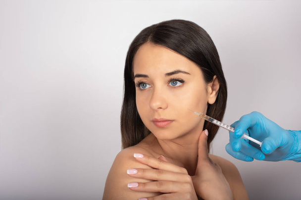 beautiful brunette girl with blue eyes, white background, beauty, syringe near the face, cosmetology - Foto, Imagen