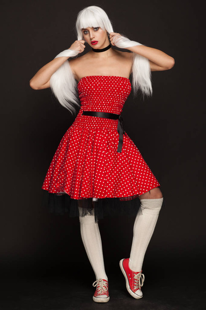 Portrait of awoman in a white wig, red dress and sneakers. Studio photo session - Foto, Bild