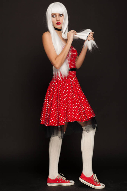 Portrait of awoman in a white wig, red dress and sneakers. Studio photo session - Фото, изображение