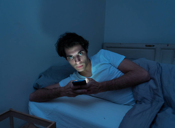 Addicted man chatting and surfing on the Internet with smart phone late at night in bed. Bored, sleepless and tired in dark room with moody light. In insomnia and mobile addiction concept. - Zdjęcie, obraz