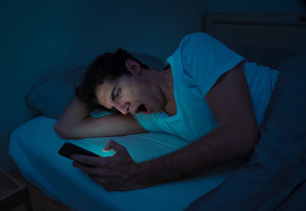 Addicted Man sohbet ve yatakta gece geç saatlere kadar akıllı telefon ile Internette sörf. Sıkılmış, uykusuz ve kasvetli ışık ile karanlık odada yorgun. Uykusuzluk ve mobil bağımlılık kavramı. - Fotoğraf, Görsel