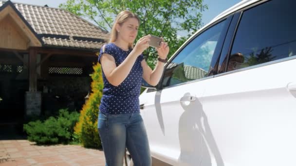 Βίντεο της νεαρής γυναίκας που φτιάχνει φωτογραφίες του αυτοκινήτου της για να το πουλήσει στο διαδίκτυο. Θηλυκό οδηγό που χρησιμοποιεί smartphone και φωτογραφίζει το όχημά της - Πλάνα, βίντεο