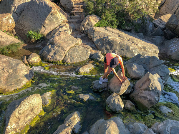 Молодая спортсменка, перелезающая через реку через скалу, спортивный момент
 - Фото, изображение