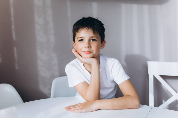Темноволосый мальчик сидит за белым столом
 - Фото, изображение