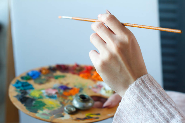 Gros plan des mains féminines dans un pull rose tenant un pinceau et une palette de peintures acryliques multicolores sur une toile blanche
 - Photo, image