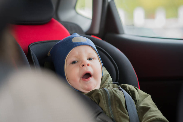 Close Up caucasian cute baby boy woke up and yawns in modern car seat. Child traveling safety on the road. Safe way to travel fastened seat belts in a vehicle with young kids. Trip with toddler. - Valokuva, kuva