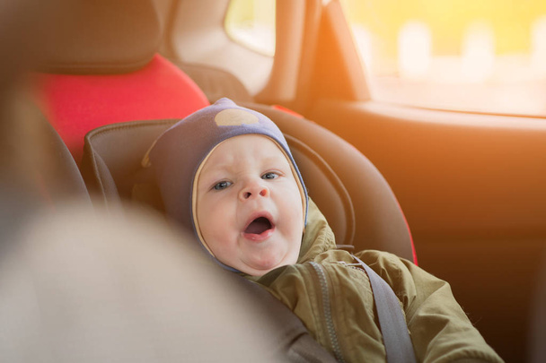 Close Up caucasian cute baby boy woke up and yawns in modern car seat. Child traveling safety on the road. Safe way to travel fastened seat belts in a vehicle with young kids. Trip with toddler. - Photo, Image