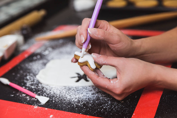 Γυναίκα διακοσμεί χριστουγεννιάτικα μπισκότα μελόψωμο με γλάσο άχνη ζάχαρη νιφάδα. Χριστουγεννιάτικο δώρο, σπιτικό μελόψωμο - Φωτογραφία, εικόνα