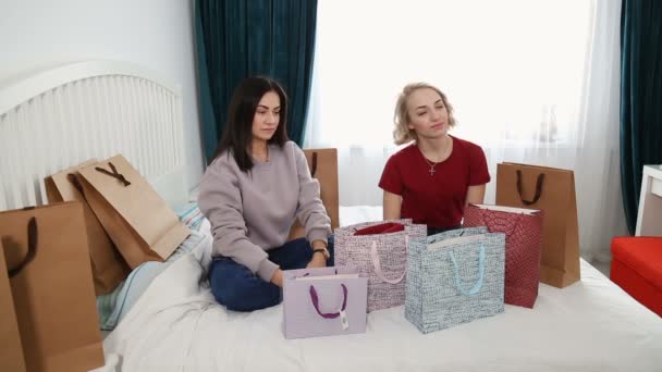 Twee aantrekkelijke vrouwen zitten op bed en bespreken nieuwe kleding van winkelen. - Video