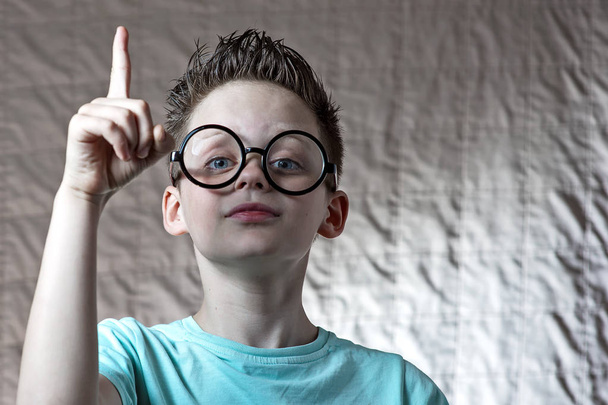 a boy in a light t-shirt and round glasses raised his index finger - Foto, imagen