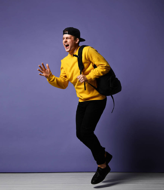 Joyful young man student with a backpack runs isolated in studio on a purple background - Photo, image