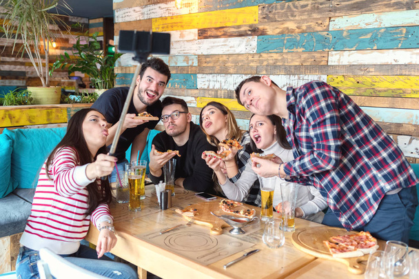 Parhaat ystävät ottavat selfien lounaskutsuilla hauskoilla kasvoilla, Happy Friendyn konsepti nuorten trendikkäiden ihmisten kanssa hauskaa yhdessä juoden olutta ja jakaen pizzaa baarissa ravintolassa
 - Valokuva, kuva