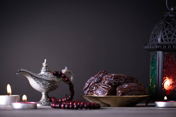 Αίσθηση φαγητού και ποτού του Ραμαζάνι. Φανάρι Ραμαζάνι με αραβική λάμπα, ξύλο Ροζάριο, τσάι, ημερομηνίες φρούτα και φωτισμό σε ένα ξύλινο τραπέζι σε σκούρο φόντο. - Φωτογραφία, εικόνα