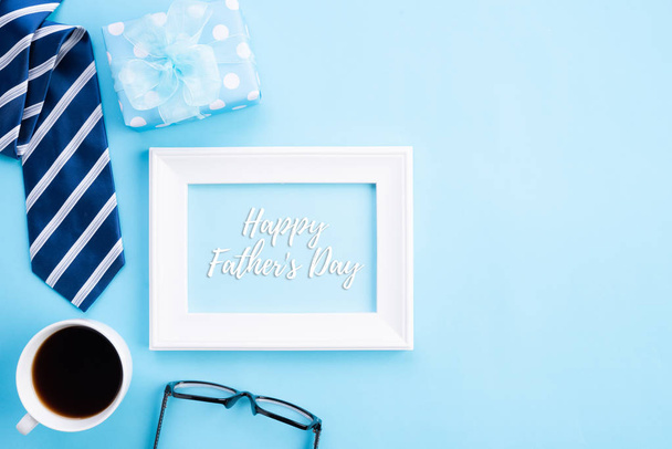 Happy Ojcowie dzień koncepcji. Widok z góry niebieski krawat, piękny prezent pudełko, kubek kawy, biała ramka na zdjęcia z szczęśliwym ojcem dzień tekst na jasnym niebieskim tle pastelowych. - Zdjęcie, obraz