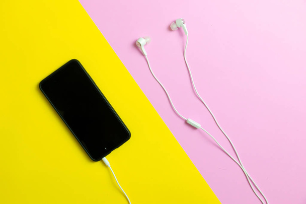 Telefony Smartphone a sluchátka poslech staré hudby na žlutém a růžovém pozadí. - Fotografie, Obrázek