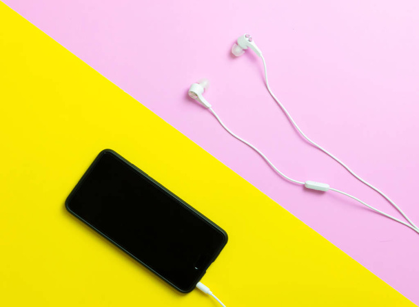 Smartphones en hoofdtelefoons luisteren naar vintage muziek op een gele en roze achtergrond. - Foto, afbeelding
