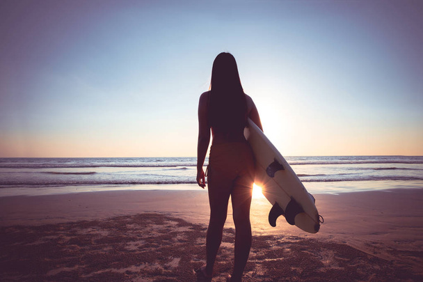 Bikinili sörfçü kadın sörf yapmaya gider. Gün batımında sahilde sörf tahtası ile güzel seksi kadın Siluet. vintage renk ton - Fotoğraf, Görsel