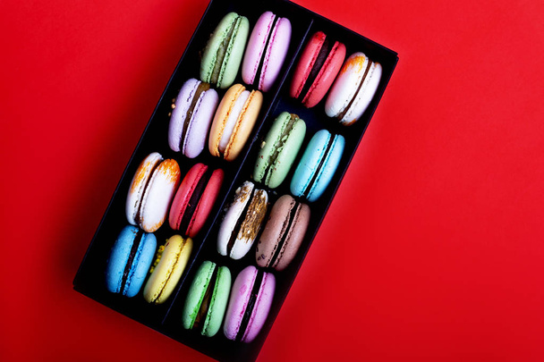Tasty different colored macarons in black box on red background - Fotoğraf, Görsel