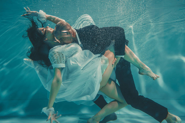 beautiful romantic couple of bride and groom after wedding swimming gently under water and relax - Foto, Imagen