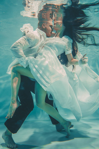 beautiful romantic couple of bride and groom after wedding swimming gently under water and relax - Foto, Bild