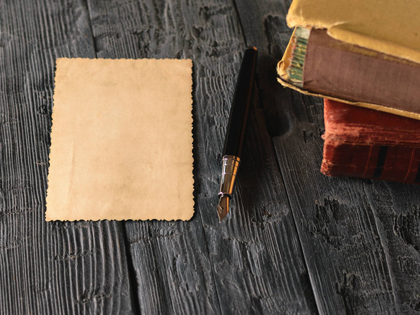 A sheet of old paper and a fountain pen with books on a wooden table. - Фото, изображение