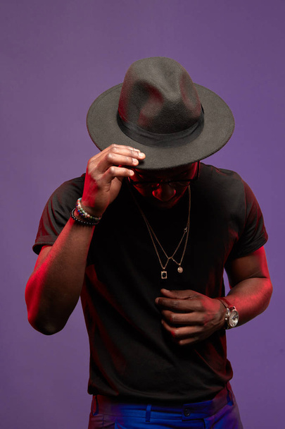 African DJ or jazz musician in hat and black t-shirt on purple background - Фото, изображение