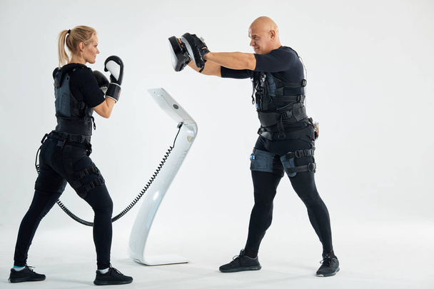 female boxer in gloves and ems suits training with a couch - Fotoğraf, Görsel