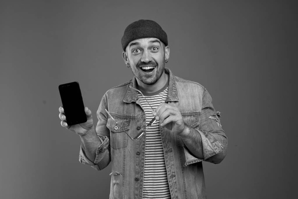 Portrait of upbeat stylish man smiling broadly while showing his smartphone - Φωτογραφία, εικόνα