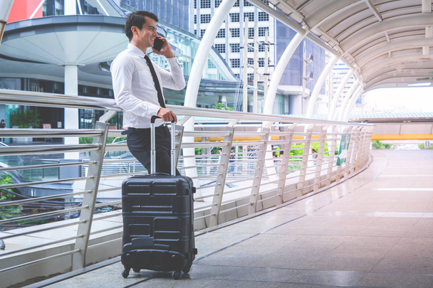Viajante turístico de negócios com bagagem está usando seu telefone celular
 - Foto, Imagem