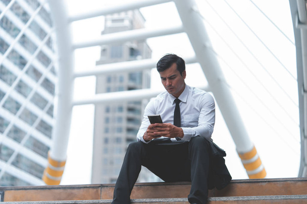 Business man is using mobile phone sitting outdoor - Photo, Image