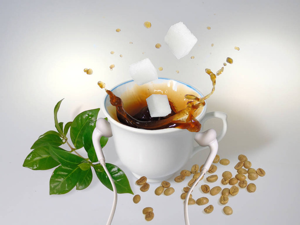                                   A white cup with white earphones put on it, splash of coffee, three  sugar cubes, green coffee beans and leaves      - Foto, afbeelding