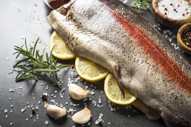 Peixe de salmão cru inteiro com ingredientes para cozinhas em preto
. - Foto, Imagem