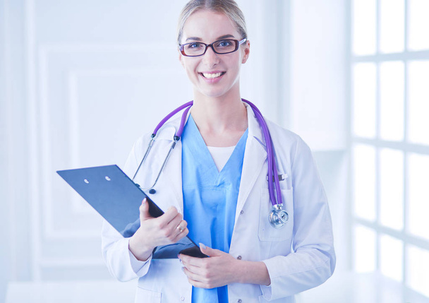 Glimlachende vrouwelijke arts met een map in uniform staand - Foto, afbeelding