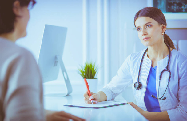 Doctor and patient discussing medical problems in a hospital consulting room. Doc filling in a patients form - Foto, Imagen