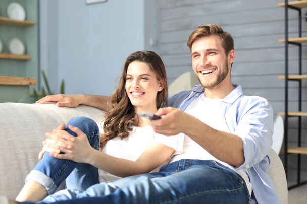 Young loving couple on sofa at home watching tv and laughing. - Photo, Image