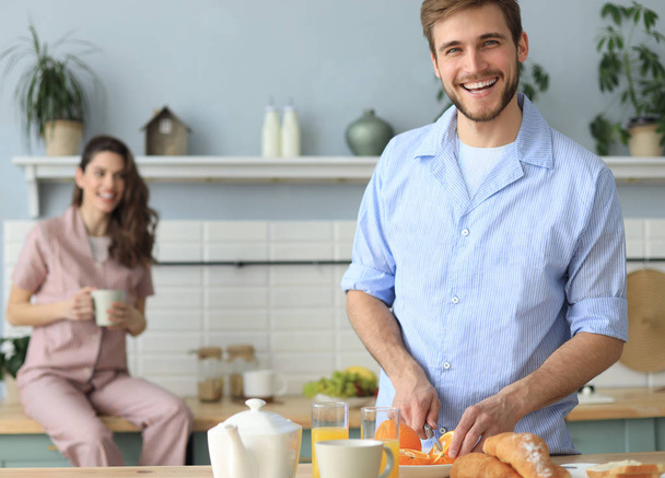 Portrait de jeune couple heureux en pyjama cuisiner ensemble dans la cuisine, boire du jus d'orange le matin à la maison
. - Photo, image