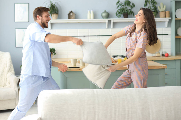 Happy loving couple having fun while having a pillow fight in the living room. - Фото, изображение