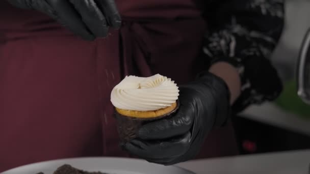 Confectioner sprinkles cupcake with chocolate. Close up view of hands in gloves. Decorating cup-cake with chocolate in slow motion. Home bakery concept. Step by step - Πλάνα, βίντεο