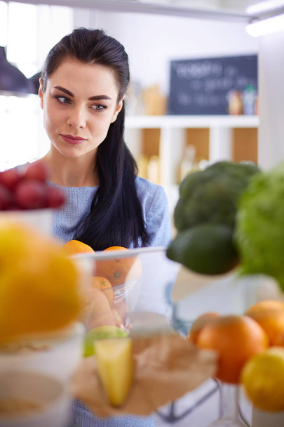 Smiling woman taking a fresh fruit out of the fridge, healthy food concept - Photo, image