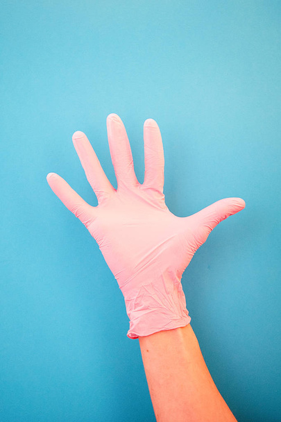 Apuntando con el dedo al número cinco, usando guantes médicos rosados, sobre un fondo azul. Buenos hábitos, vacunación, tienda médica, farmacia
. - Foto, imagen
