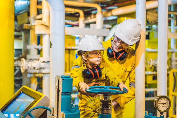 Young man and a little boy are both in a yellow work uniform, glasses, and helmet in an industrial environment, oil Platform or liquefied gas plant - Photo, Image