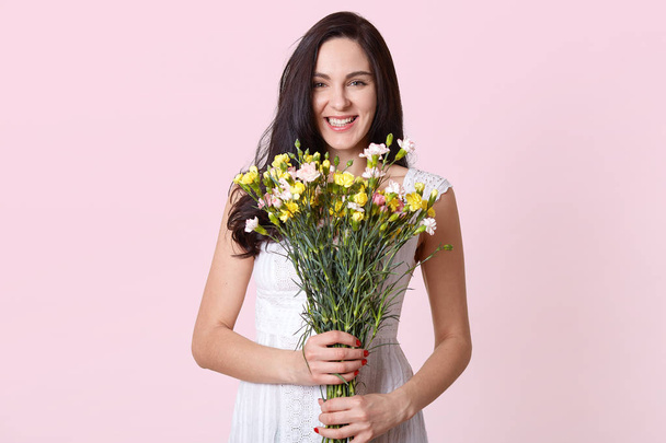 Image of girl holding bouquet of flowers in the hands, chorming lady expresses happyness, looking directly at camera, being in good mood on her birthday. Copy space for promotion or advertisment. - Fotoğraf, Görsel