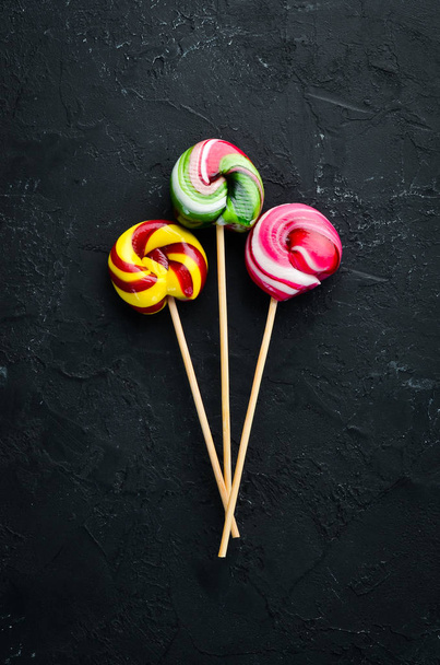 Caramel candies and lollipops. Colored candies. On a black background. Top view. free copying space. - Foto, Bild